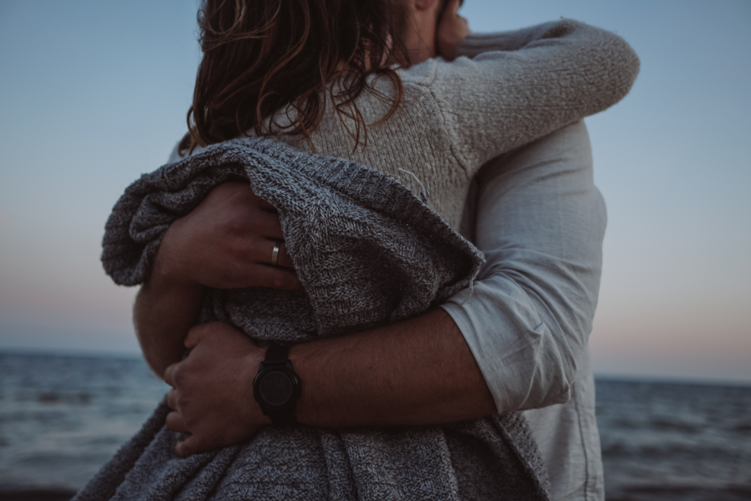 Couple embracing by the ocean at sunset, illustrating comfort and quiet expressions of love